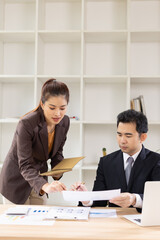 Two Asian business people with analyzing financial report working together in office.