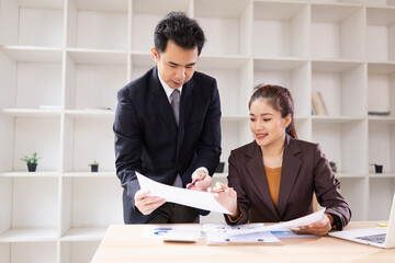 Two Asian business people with analyzing financial report working together in office.