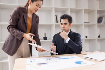 Asian businesswoman and businessman are holding paper documents financial analysis data charts in office working space.