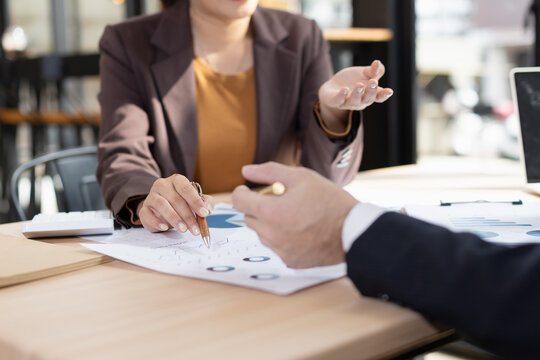 Asian businesswoman and businessman are holding paper documents financial analysis data charts in office working space. - Powered by Adobe