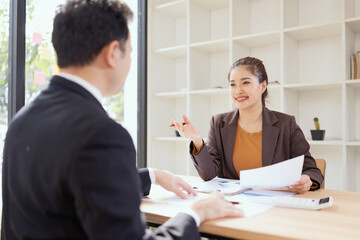 Asian businesswoman and businessman are holding paper documents financial analysis data charts in office working space.