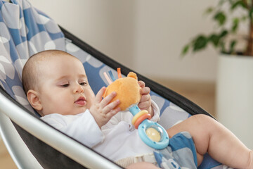 Baby playing with rattle toy in baby bouncer. Baby care.