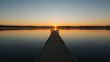 Obraz premium A serene sunset casts a warm glow over a tranquil lake, viewed from a deserted wooden dock.