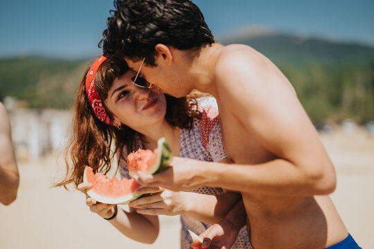 A young couple enjoys sharing a refreshing watermelon outdoors on a sunny day, creating a joyful and vibrant moment. Perfect image depicting happiness, and leisure in a charming summer atmosphere. - Powered by Adobe