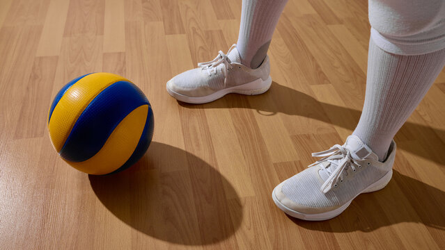 Athlete holding volleyball on indoor wooden court highlighting sportsmanship. Concept of match preparation, sports still life, volleyball floor context, and athlete focus storytelling.