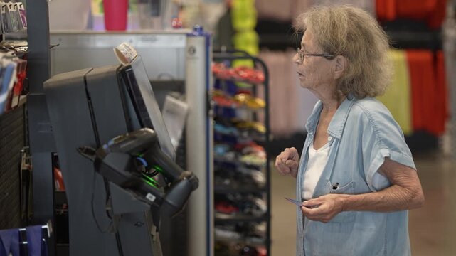 Senior woman with a walker uses a self checkout kiosk at a hardware store while shopping for home improvement supplies and decor.