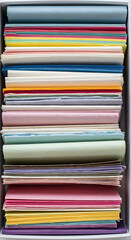 Stacked pastel paper sheets in a white box, top-down view, craft supplies