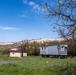 A construction trailer on wheels in a field near the hills.