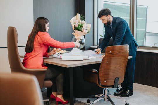 A professional man and woman working on a project in a modern office with a bouquet of flowers. They are engaged in productive discussion. - Powered by Adobe