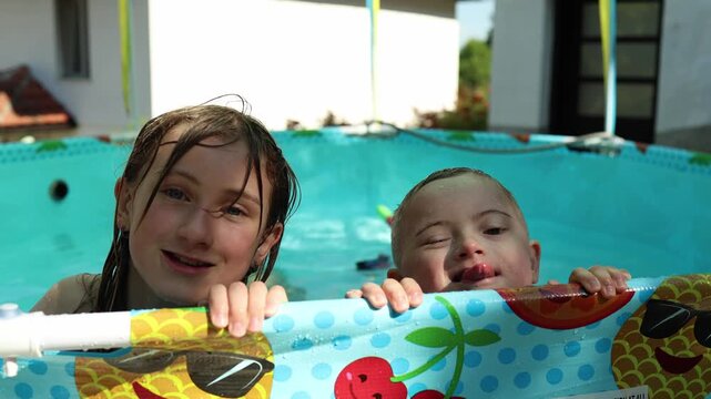 Two children in the pool are laughing, enjoying and mocking the camera. A boy with Down syndrome plays with sister. Fun, summer, vacation. 