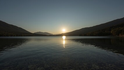 Fototapeta premium Serene sunset over a tranquil lake, reflecting mountains and a golden sky.
