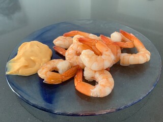Closeup image of prawns served with cocktail sauce on a round glass plate