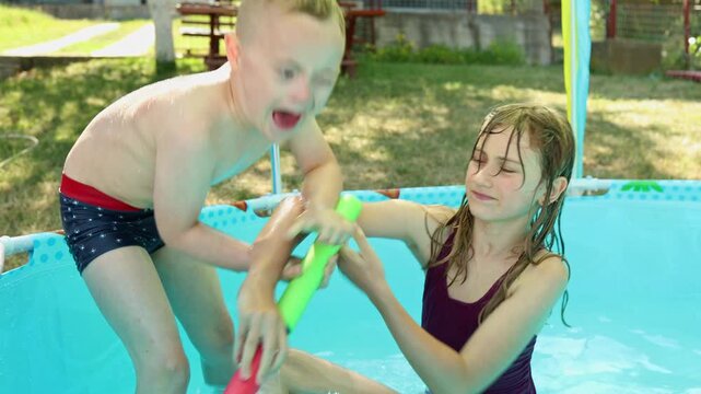Cute authentic family moments. Sweet boy with Down syndrome plays and fight in a little pool with his sister. Family country side vacation. Summer. 