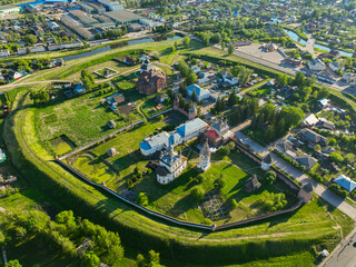 A wide aerial view presents the ancient city center of Yuryev Polsky, Russia, with its historical buildings enclosed by a protective earthen rampart, surrounded by modern urban development