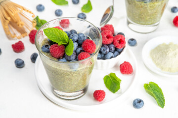 Healthy breakfast chia pudding with with matcha latte tea and fresh summer berries in glasses, white background copy space