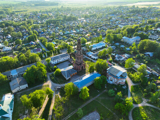An aerial panoramic view of Yuryev Polsky, Russia, showcasing the city's residential areas and a prominent historic bell tower rising from the green urban landscape
