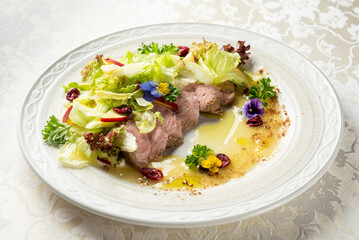 Gourmet sliced meat with fresh salad, apple slices, cranberries, and edible flowers on a decorative...