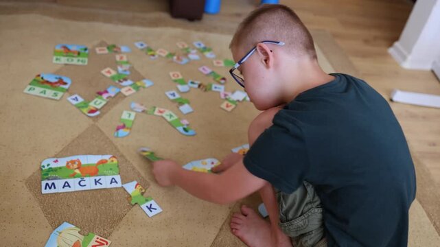  A boy with Down syndrome playing with puzzle at home. Cute kid, school, education, diverse people, candid family moments. Real, authentic people. 