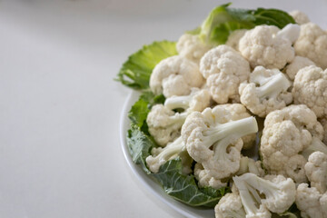 Fresh and raw cauliflower on the white plate.  The cauliflower  -  vegetable is cut into pieces on white background. The vegetable is divided into inflorescences on the plate