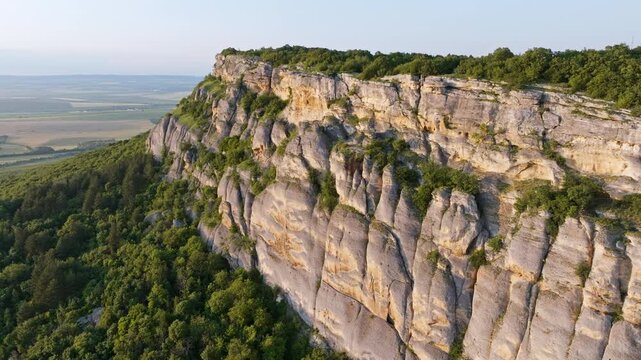 Flying over Madara Rider, ancient rock relief in Bulgaria Shumen Province, drone view of cultural monument and nature, green forests and fields, limestone plateau, summer sunlight enhances historical