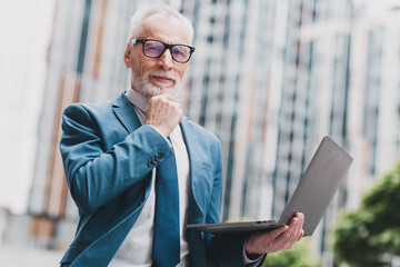 Successful mature businessman outdoors holding a laptop, representing leadership, professionalism