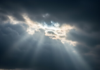 Stunning view of bright sun rays shining through a break in dark, ominous storm clouds, creating a dramatic and hopeful scene.