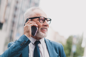 Successful senior businessman in a suit using a smartphone outdoors in a city setting during a...