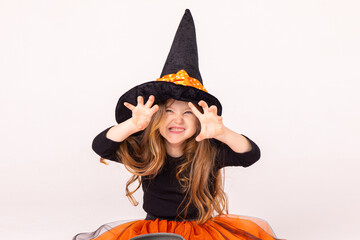 Happy funny child girl in witch costume on Halloween makes horror face and grimaces on white...