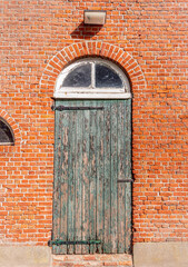 Door with peeling green paint in the brick wall of an old barn. The photo was taken in the...