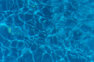 Close-up view of sunlit ripples and reflections on the surface of a clear blue swimming pool, creating an abstract, calming water pattern ideal for summer, relaxation, and vacation themes