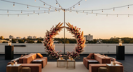 An elegant rooftop wedding ceremony setup with a large circular floral arch under string lights during a beautiful sunset.