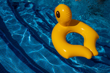 Bright yellow inflatable duck ring floating alone in a clear blue swimming pool, creating a playful...
