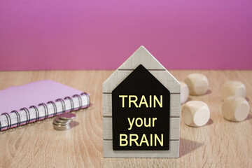Train Your Brain on a black board. Beautiful purple background. Notebook and silver coins on the...