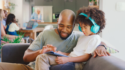 Father And Son Using Digital Tablet At Home With Multi-Generation Family In Background