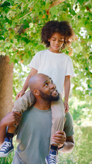 Father And Son In Summer Garden With Boy Riding On Dads Shoulders