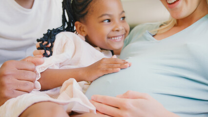 Close Up Of Family With Daughter Cuddling Pregnant Mother At Home Together