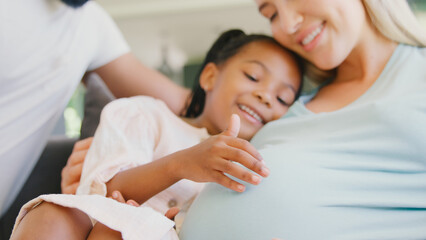 Close Up Of Family With Daughter Cuddling Pregnant Mother At Home Together