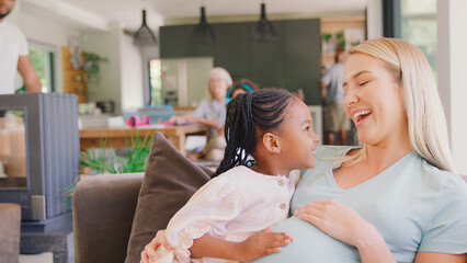 Family With Daughter Cuddling Pregnant Mother At Home Together