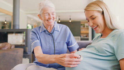 Senior Midwife With Stethoscope Visiting Pregnant Woman At Home With Family In Background
