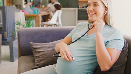 Pregnant Woman At Home Listening To Baby Heartbeat With Stethoscope