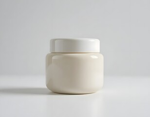 A simple cream jar with a white lid on a white surface in a minimalist studio setting with soft lighting