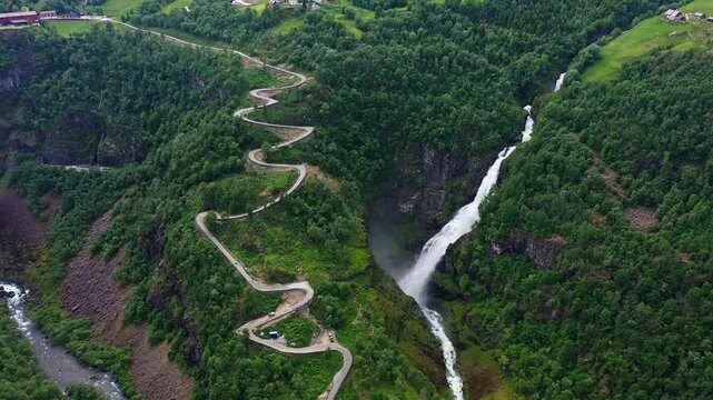 Aerial view of the cascading Stalheim waterfall contrasting sharply with the winding road, nestled among the lush green forests, Stalheim, Norway.