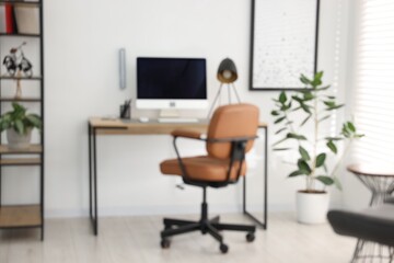 Blurred view of workplace with wooden desk, lamp and computer indoors