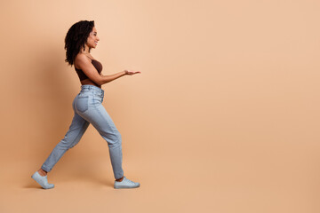 Confident young woman walking in casual style against beige background, showcasing trendy fashion...