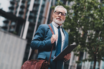 Confident mature businessman standing outdoors holding clipboard, showcasing professional attire...