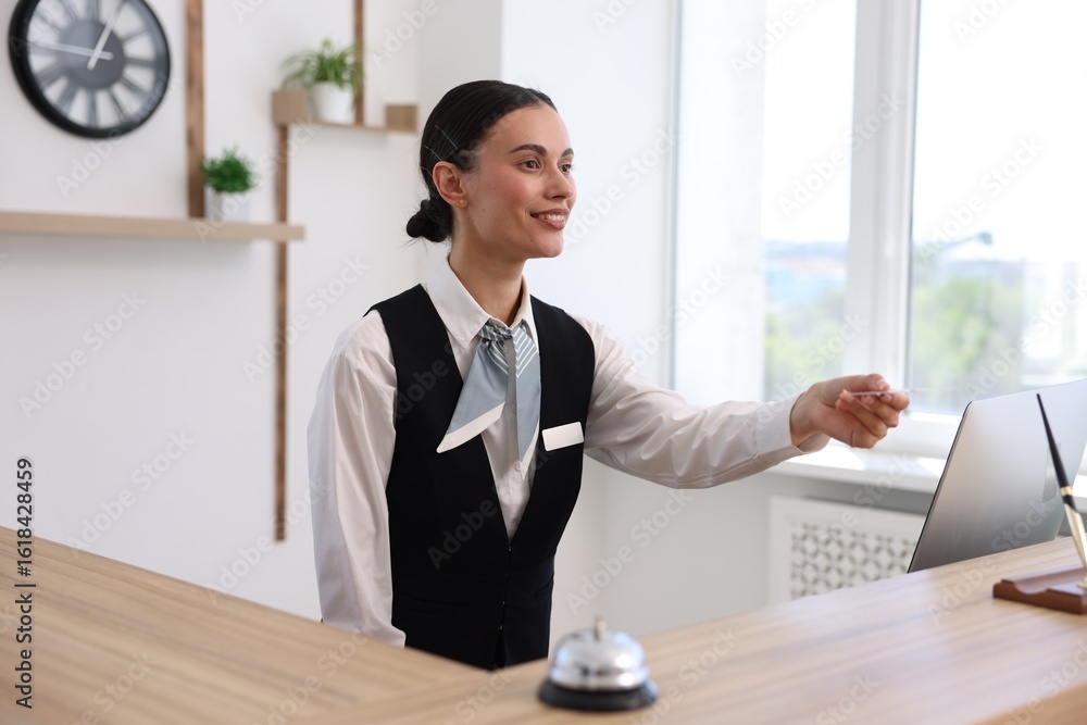 Poster smiling receptionist in uniform giving card key at reception desk in hotel