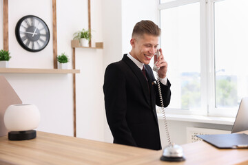 Smiling receptionist talking with client by phone at reception desk in hotel