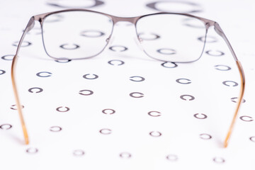 A pair of eyeglasses with a gold frame and a black lens. The frame is made of metal and has a brown tint. The eyeglasses are placed on a white background with a pattern of circles
