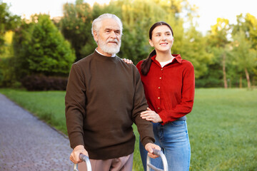 Smiling caregiver supporting elderly man who using walking frame outdoors