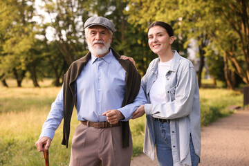 Smiling caregiver supporting elderly man with walking cane outdoors